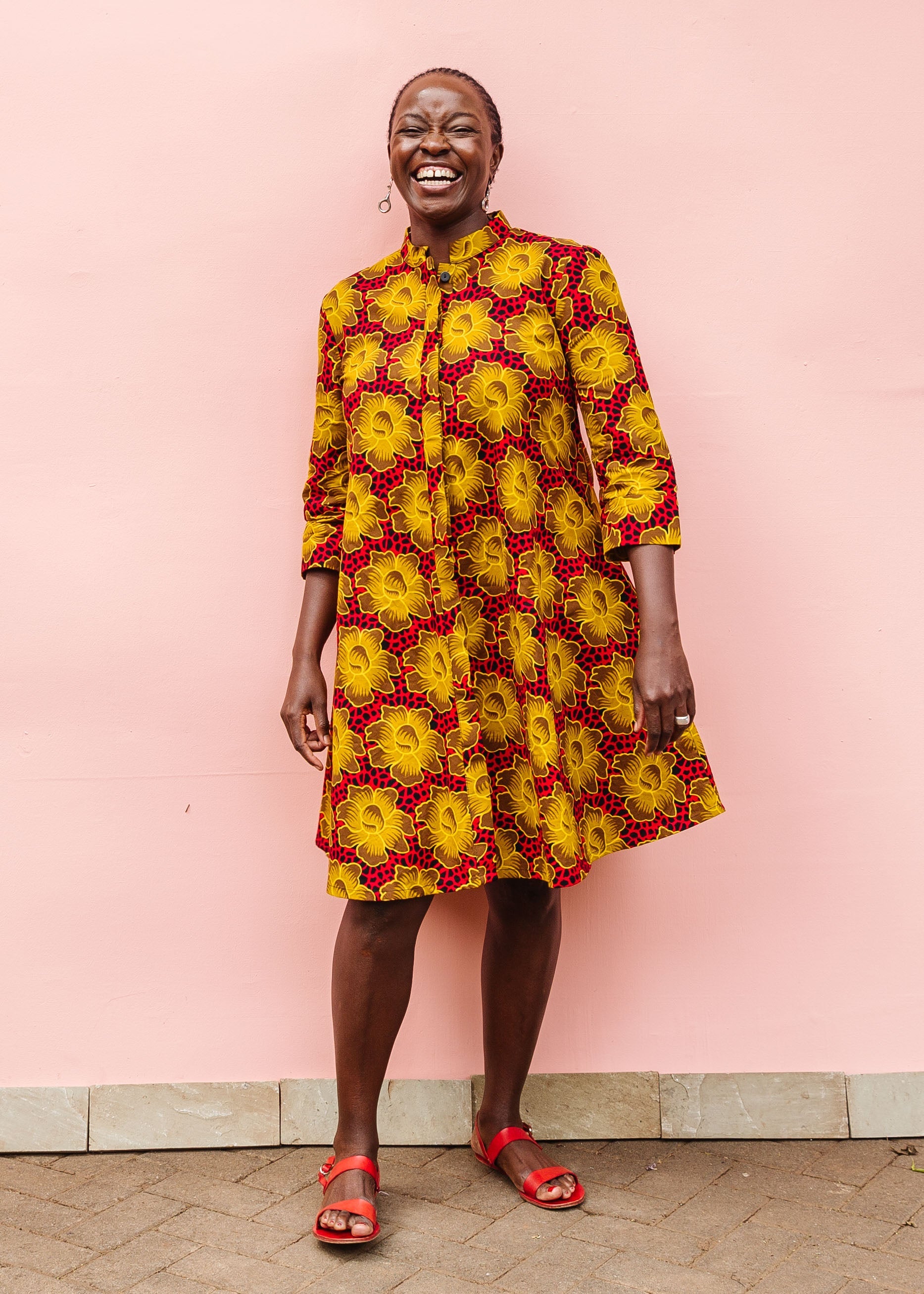 Model wearing red dress with yellow and brown flowers.
