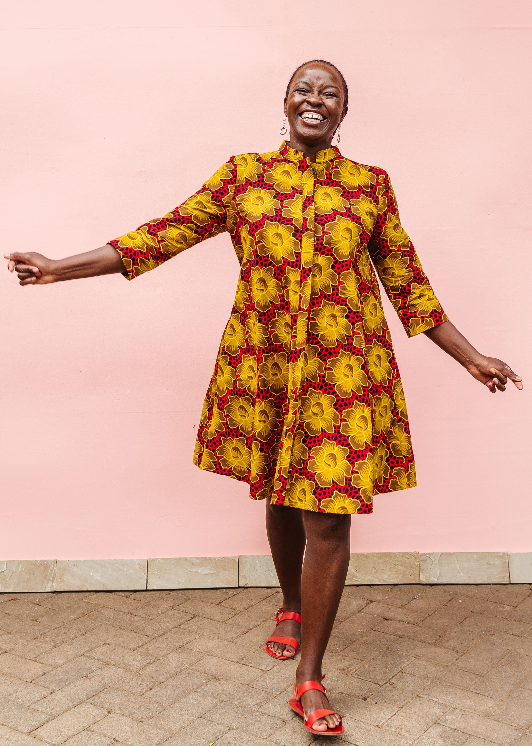 Model wearing red dress with yellow and brown flowers.