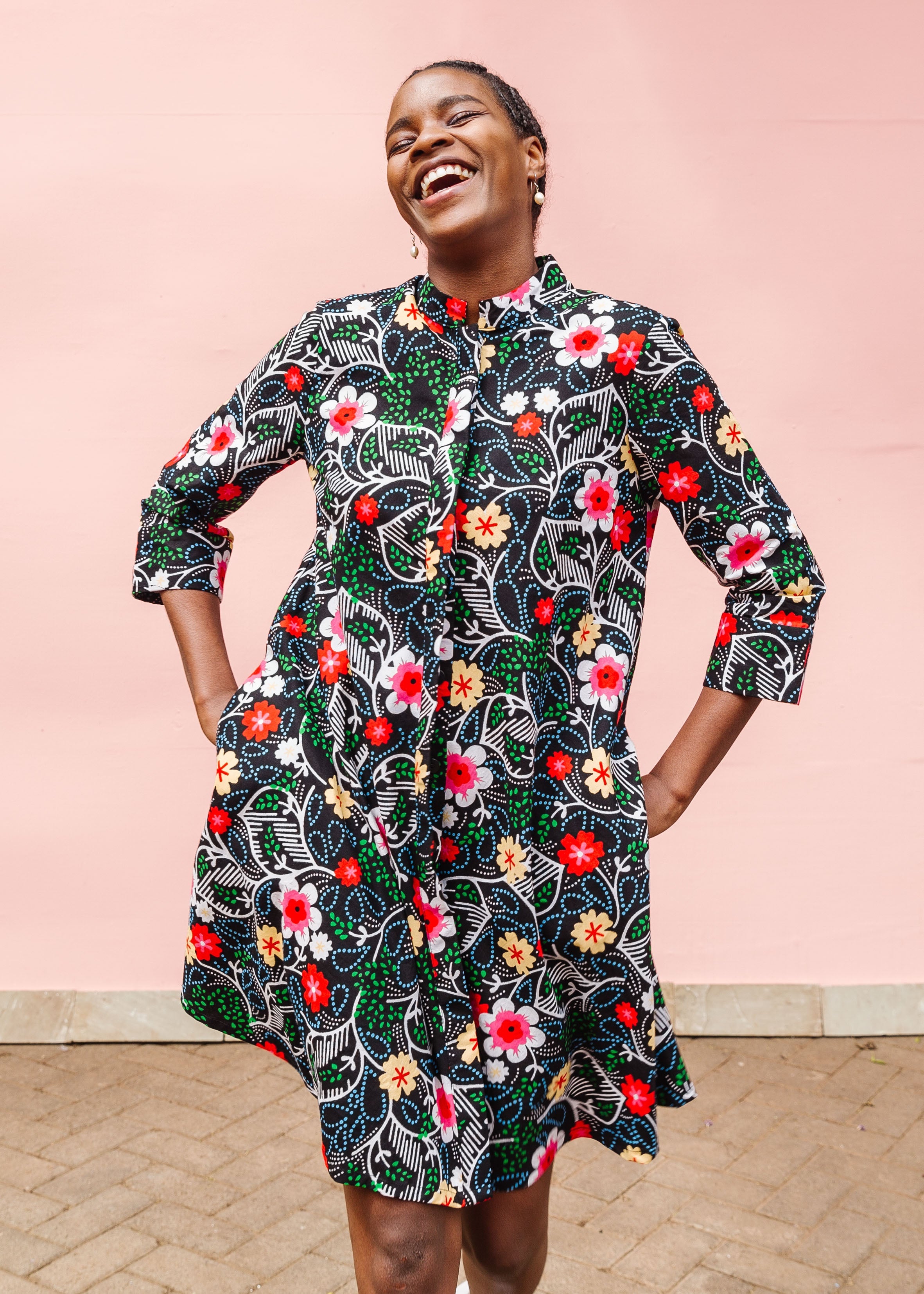 Model wearing black dress with white, green, red and yellow floral print.