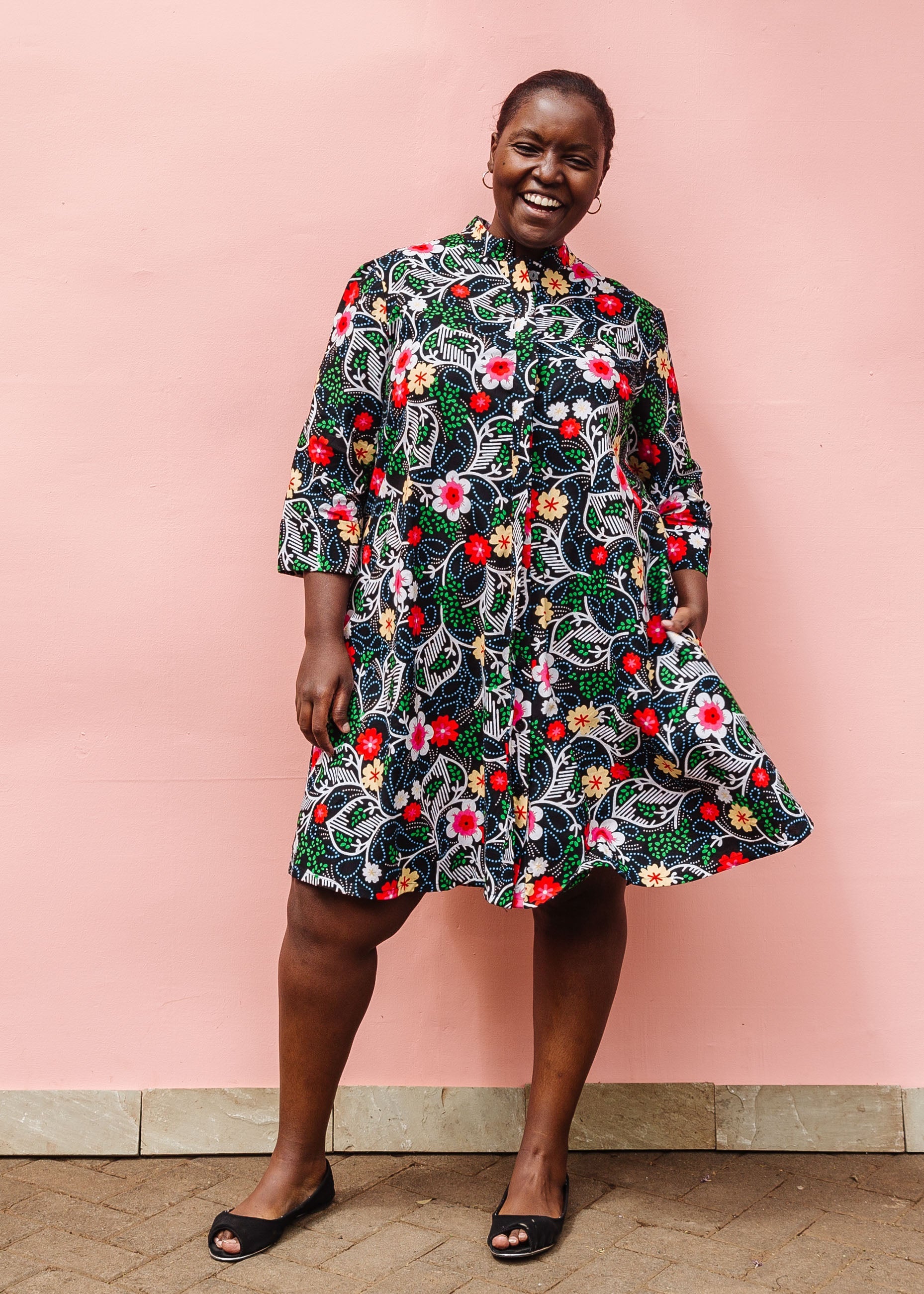 Model wearing black dress with white, green, red and yellow floral print.