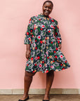Model wearing black dress with white, green, red and yellow floral print.