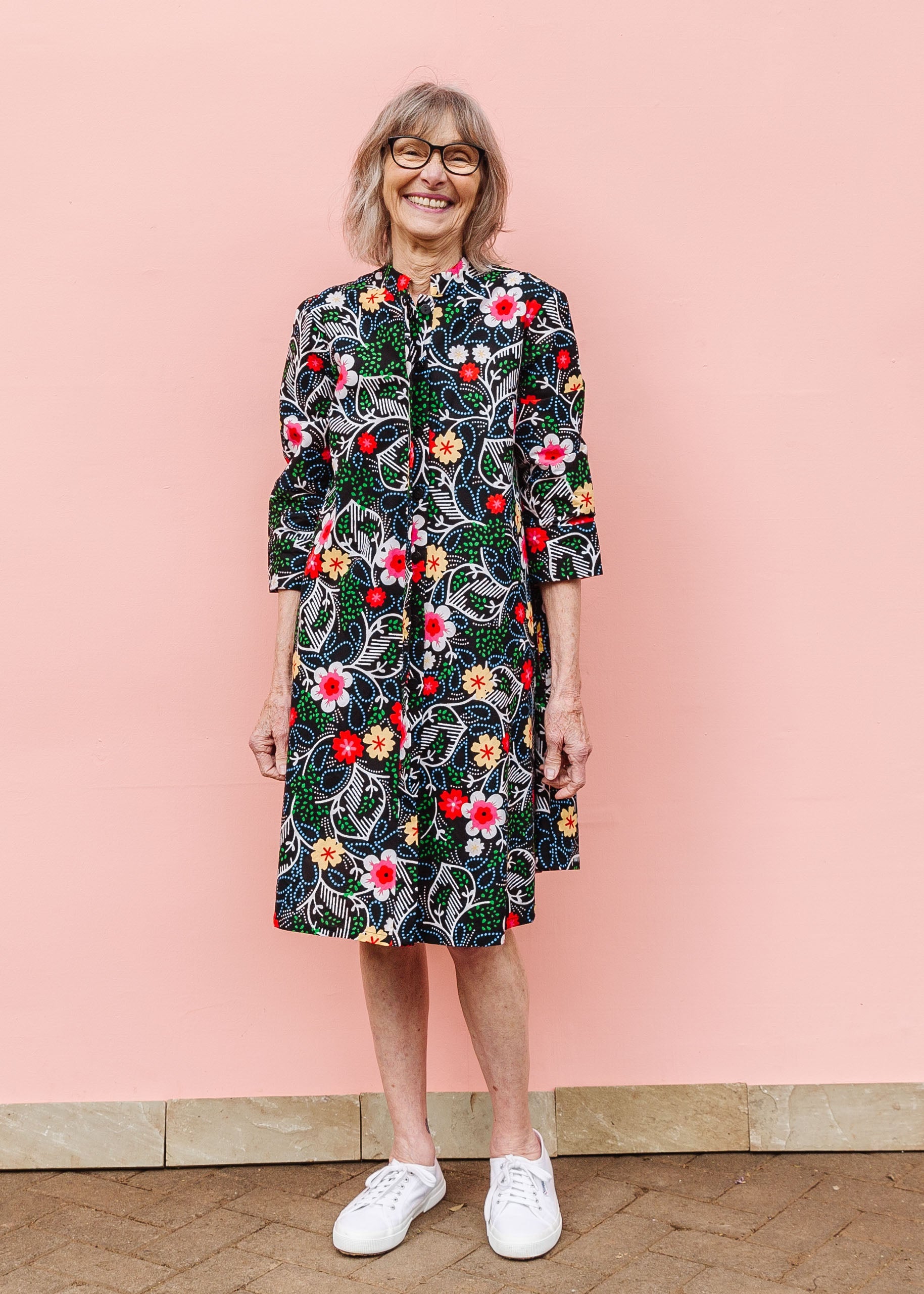 Model wearing black dress with white, green, red and yellow floral print.