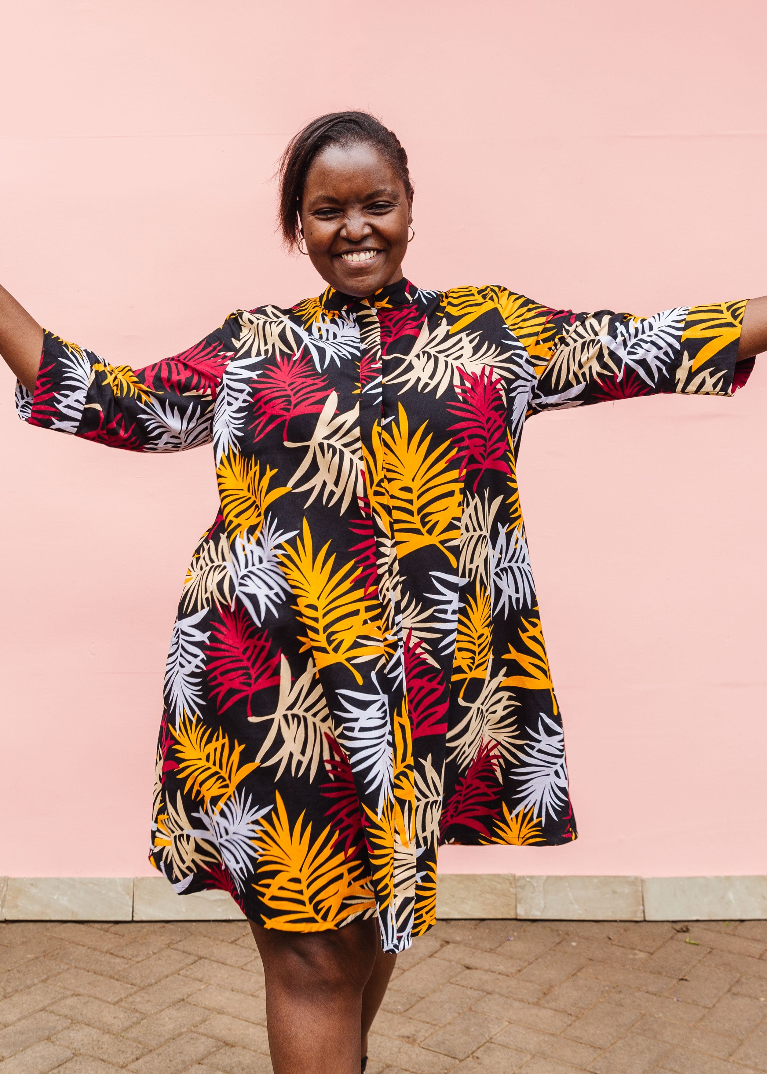 Model wearing black dress with orange, red and white leaf print.
