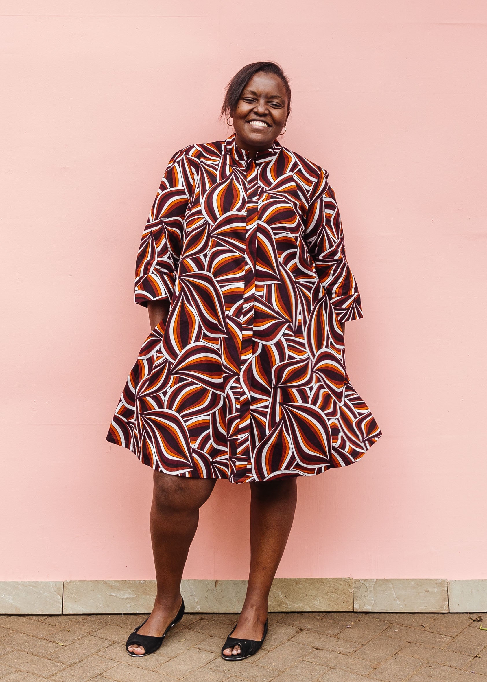 Model wearing brown, orange, burgundy and white abstract print dress.