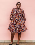 Model wearing brown, orange, burgundy and white abstract print dress.