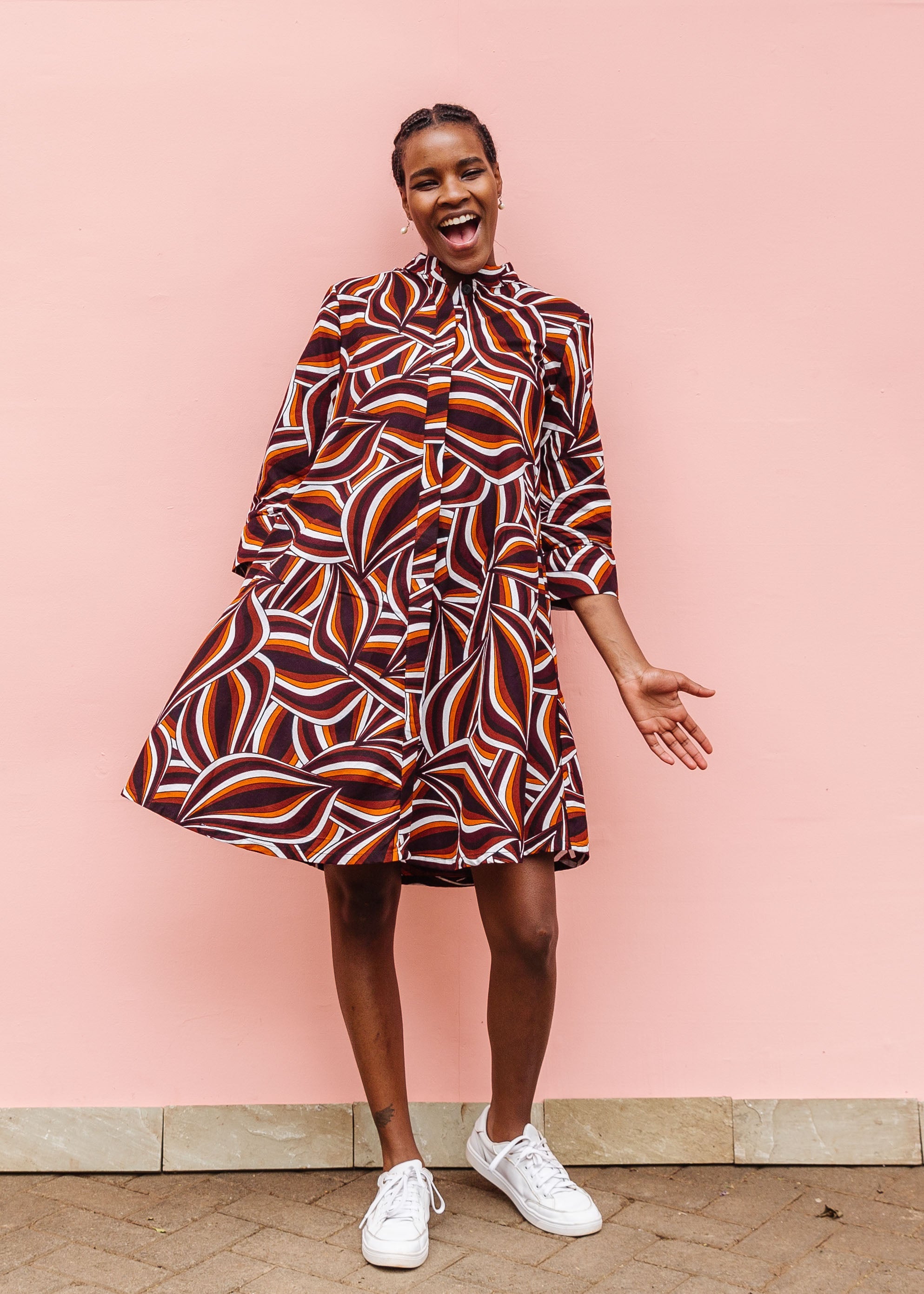 Model wearing brown, orange, burgundy and white abstract print dress.