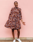 Model wearing brown, orange, burgundy and white abstract print dress.