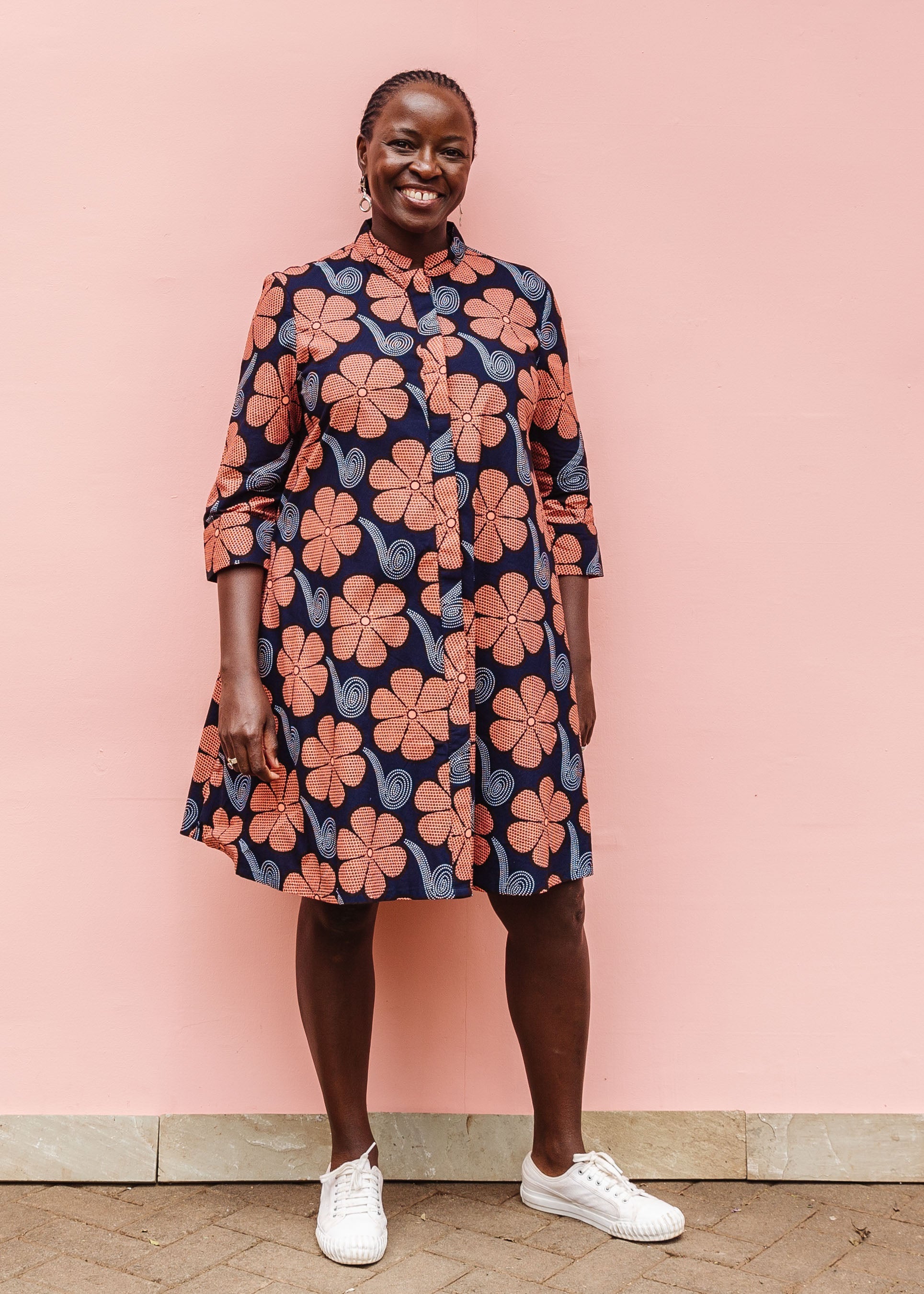 Model wearing navy dress with brown flowers and white swirls.