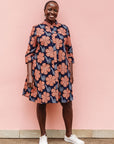 Model wearing navy dress with brown flowers and white swirls.