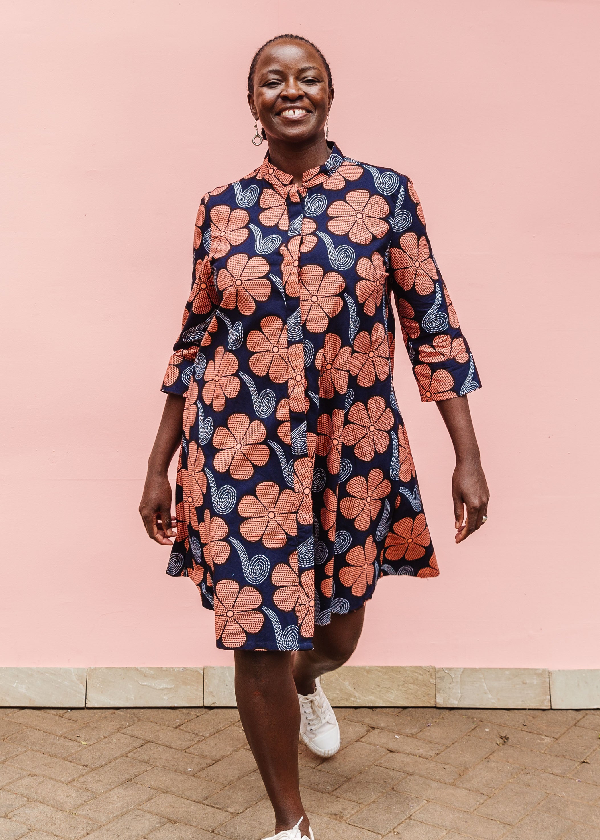 Model wearing navy dress with brown flowers and white swirls.