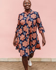 Model wearing navy dress with brown flowers and white swirls.