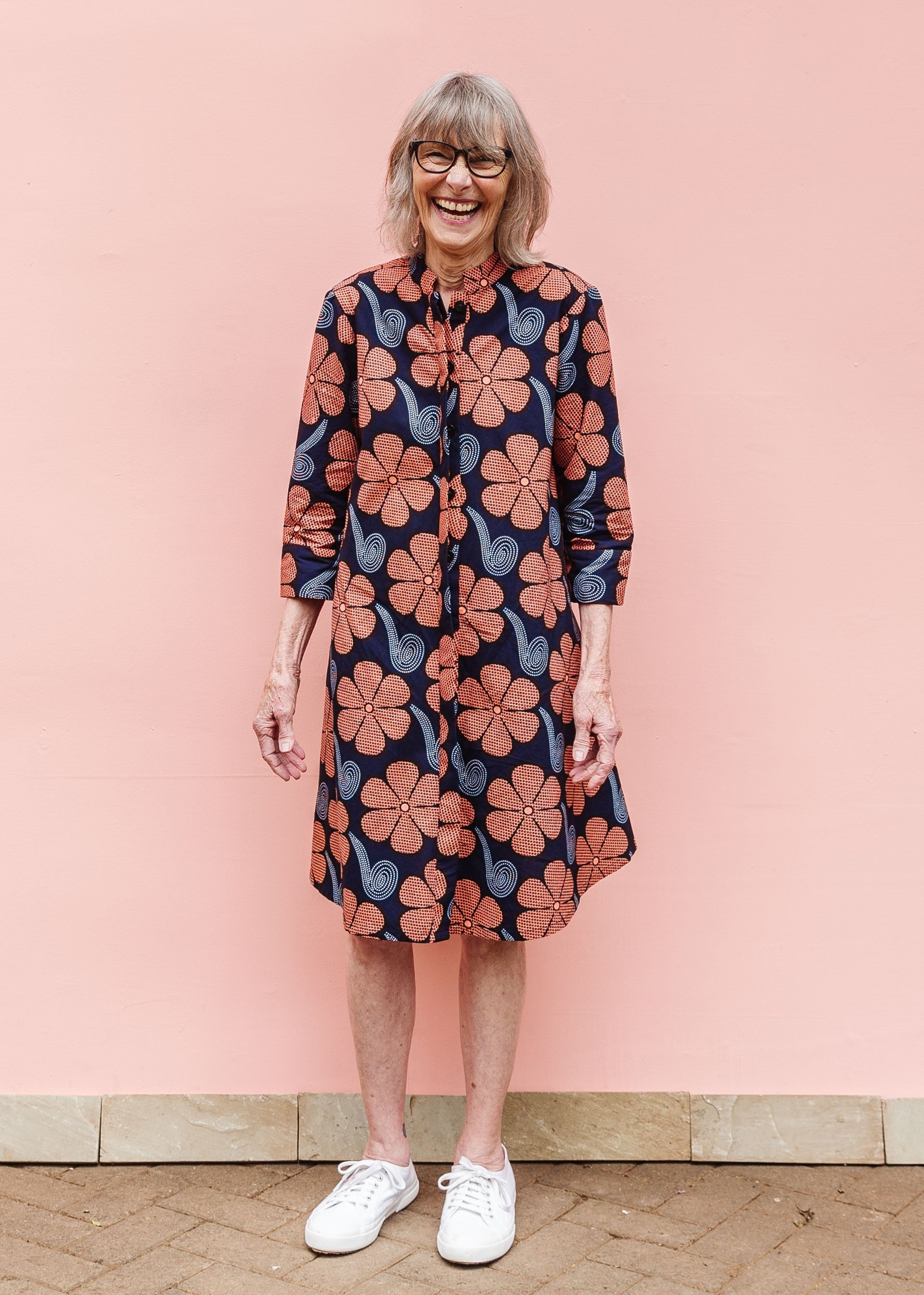 Model wearing navy dress with brown flowers and white swirls.
