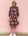 Model wearing navy dress with brown flowers and white swirls.