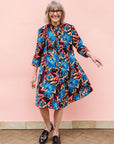 Model wearing black dress with blue, beige and red splatter print.