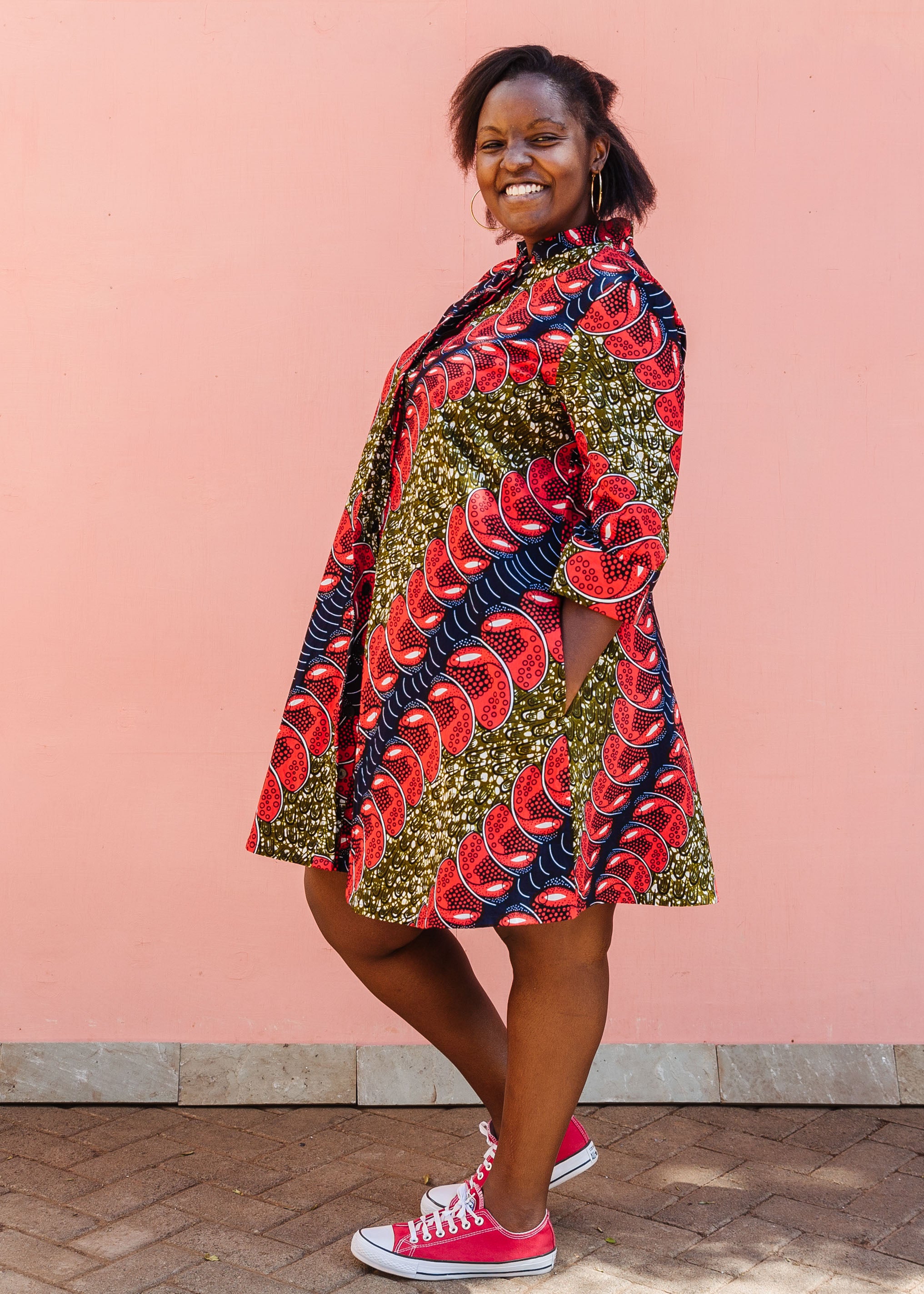 Model wearing green dress, with bold red and navy bauble print.