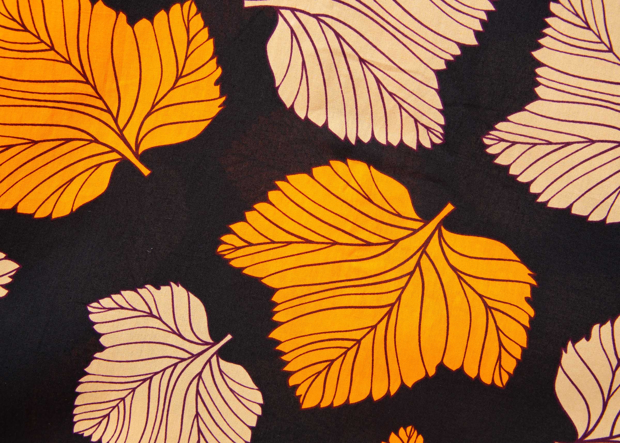 Close up display of orange, beige and black leaf print dress.