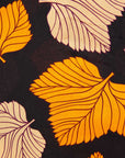 Close up display of orange, beige and black leaf print dress.