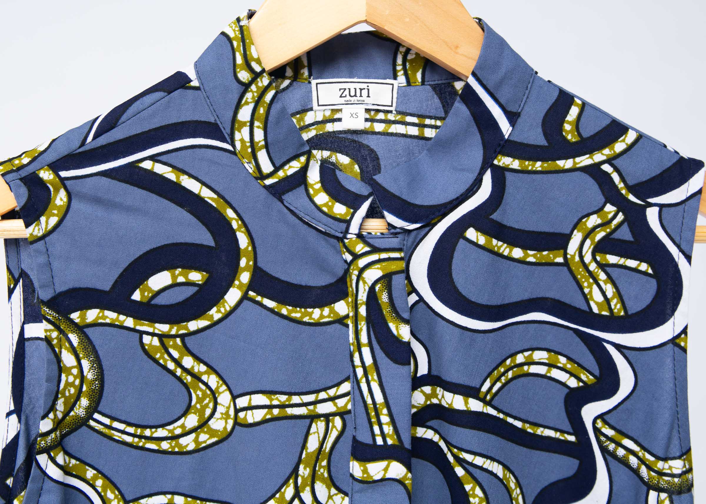Display of blue sleeveless dress with green, white and navy squiggle design.