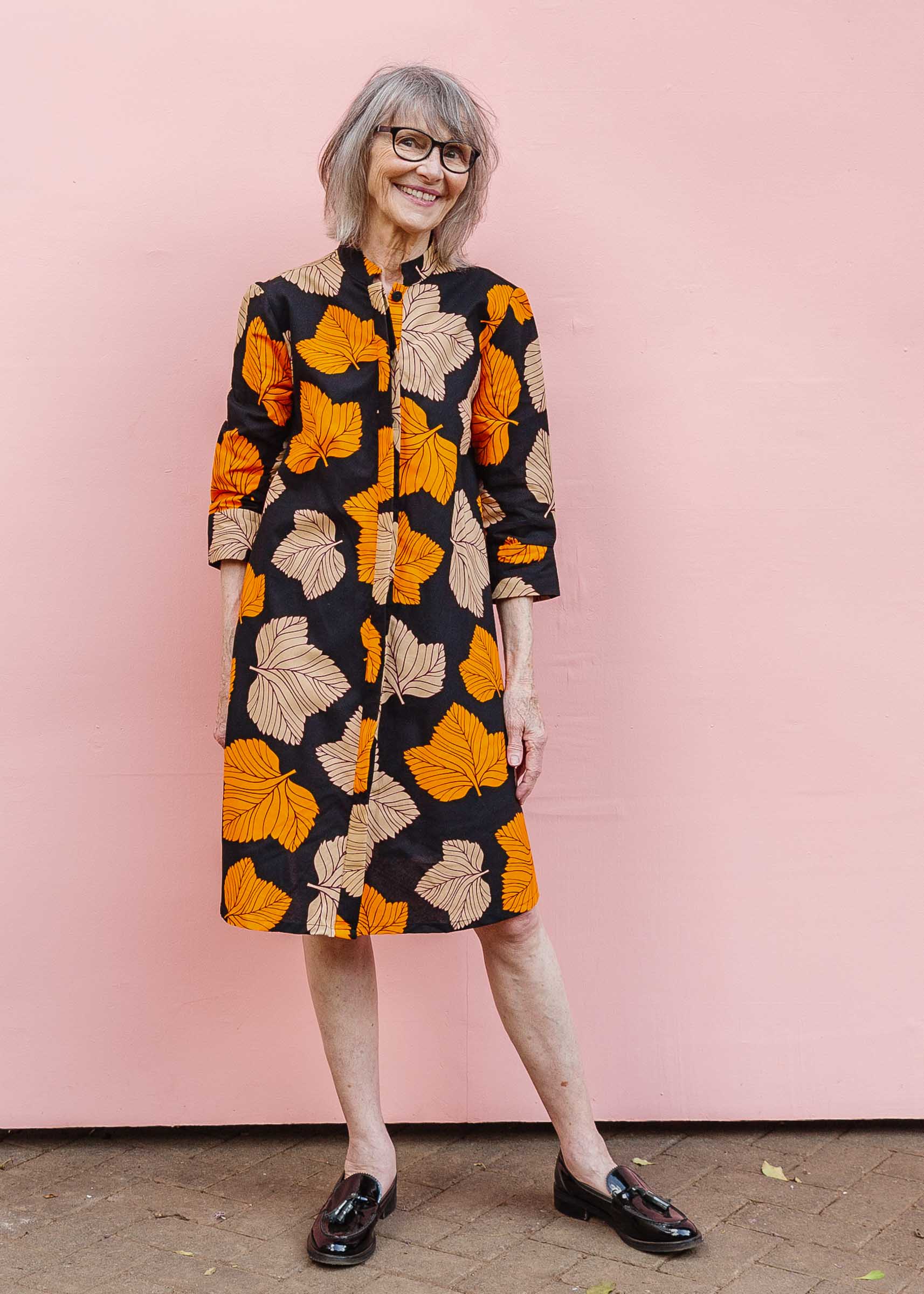 Model wearing orange, beige and black leaf print dress.