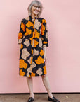 Model wearing orange, beige and black leaf print dress.