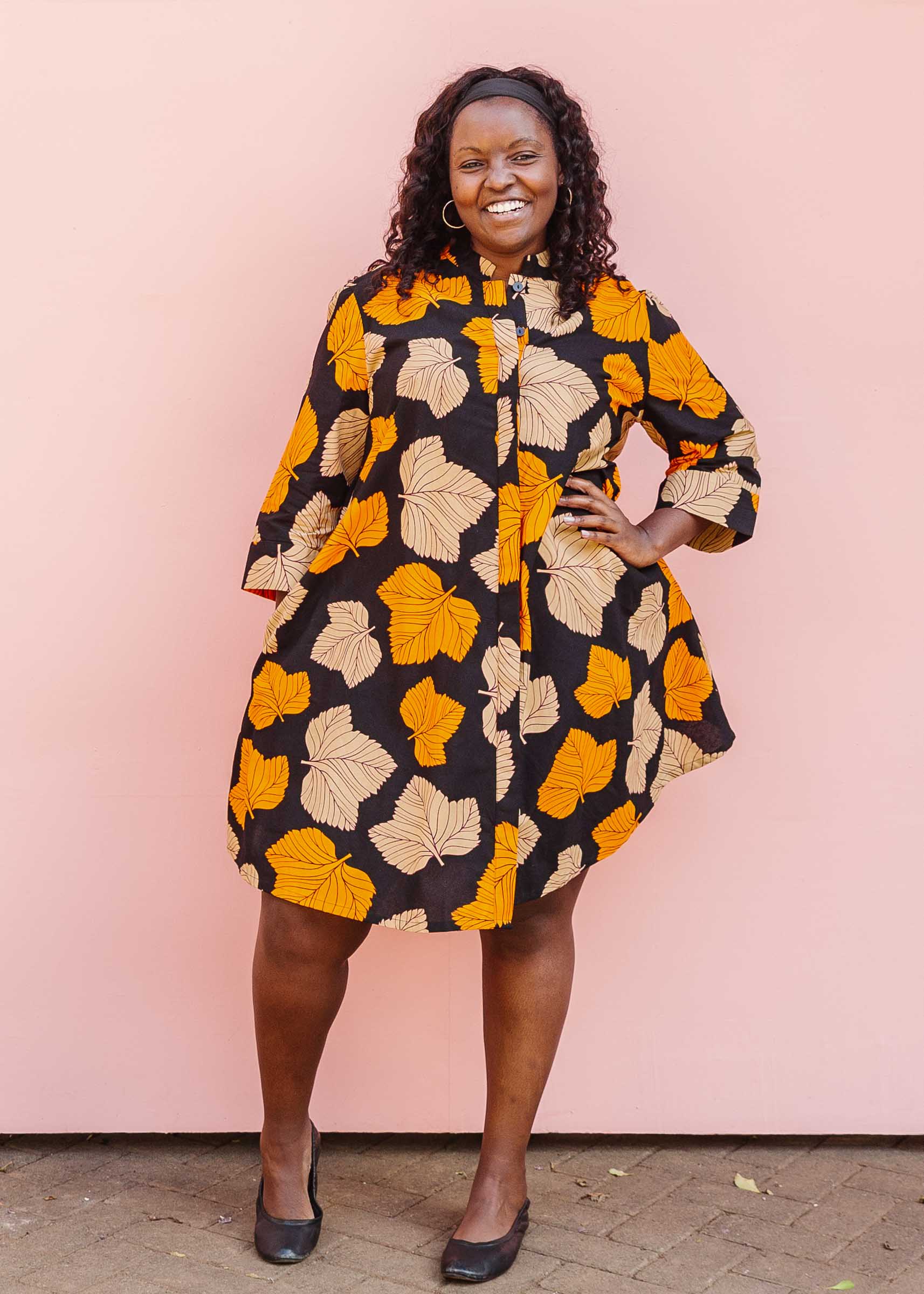 Model wearing orange, beige and black leaf print dress.