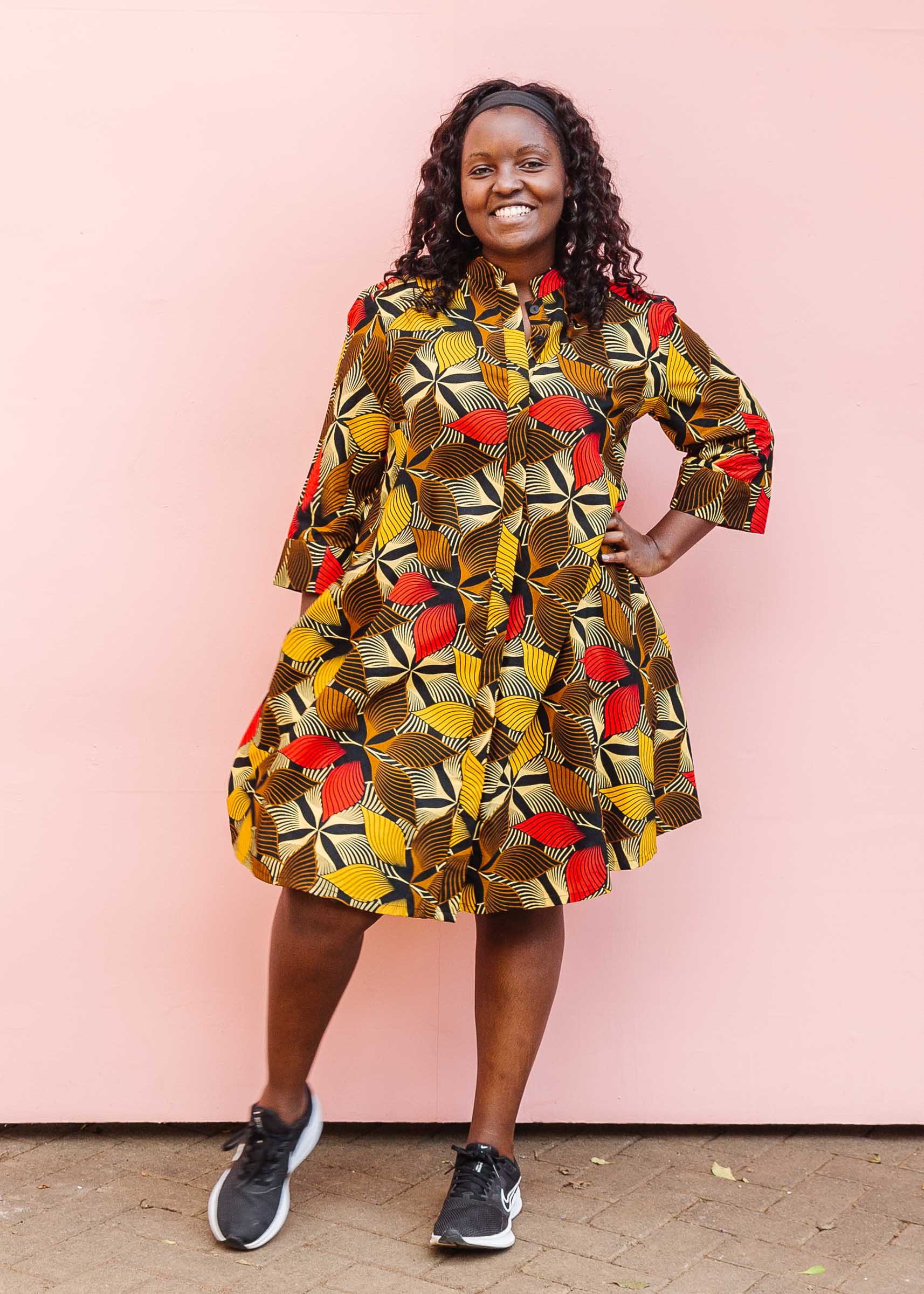 The model is wearing brown, yellow, red and black leaf print dress.