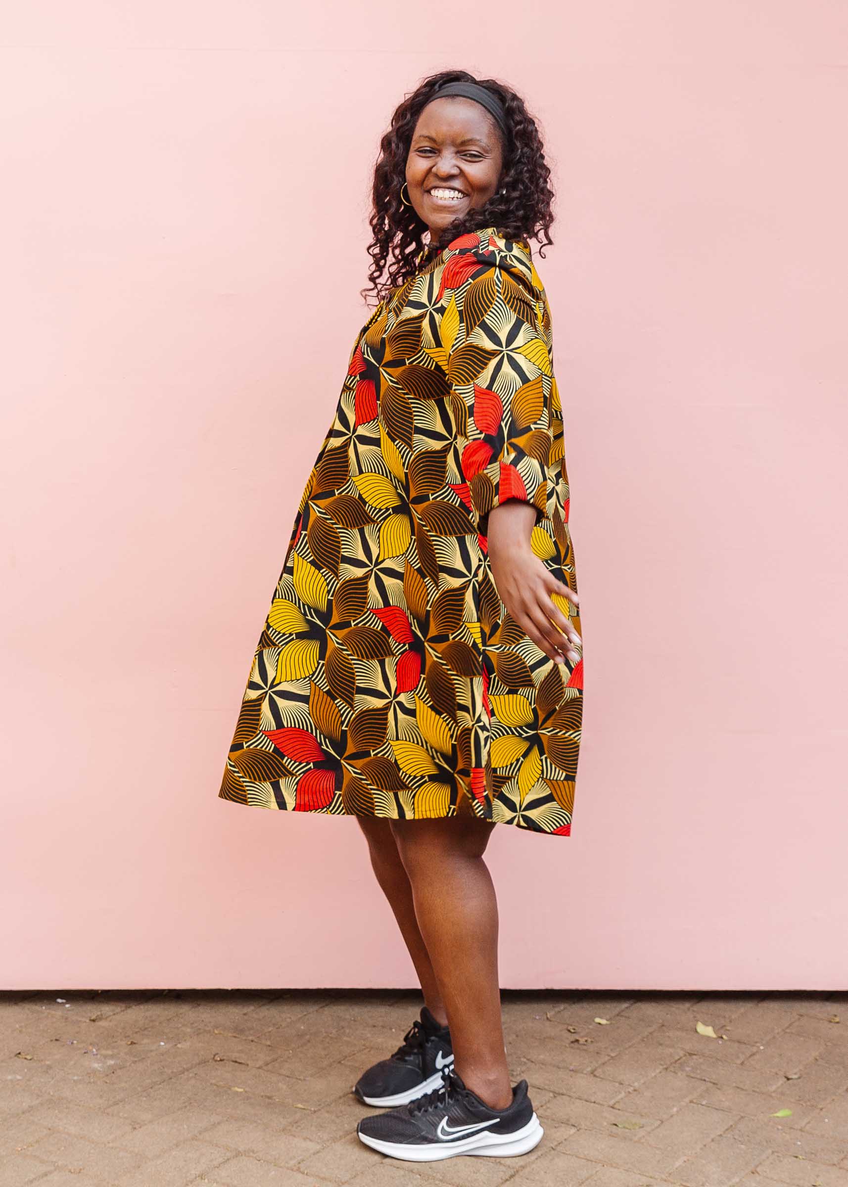 The model is wearing brown, yellow, red and black leaf print dress.
