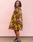 The model is wearing brown, yellow, red and black leaf print dress.