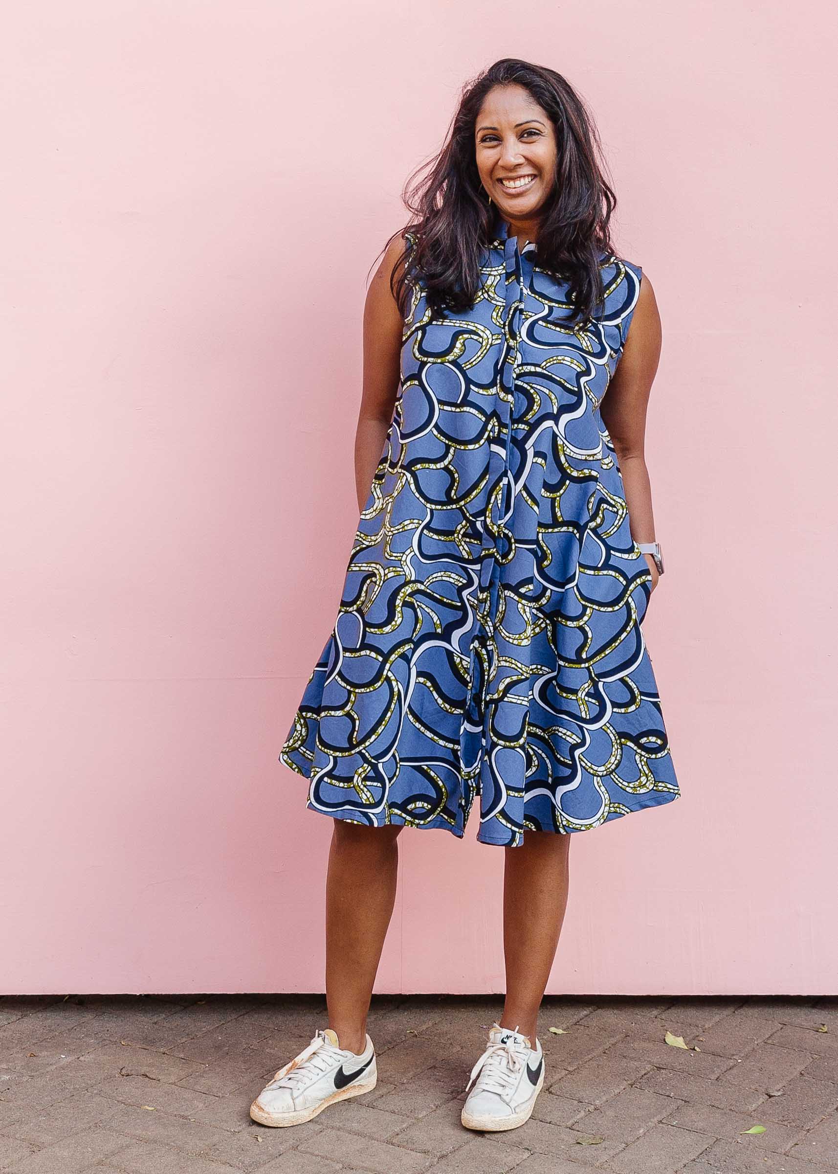 Model wearing blue sleeveless dress with green, white and navy squiggle design.
