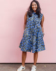 Model wearing blue sleeveless dress with green, white and navy squiggle design.