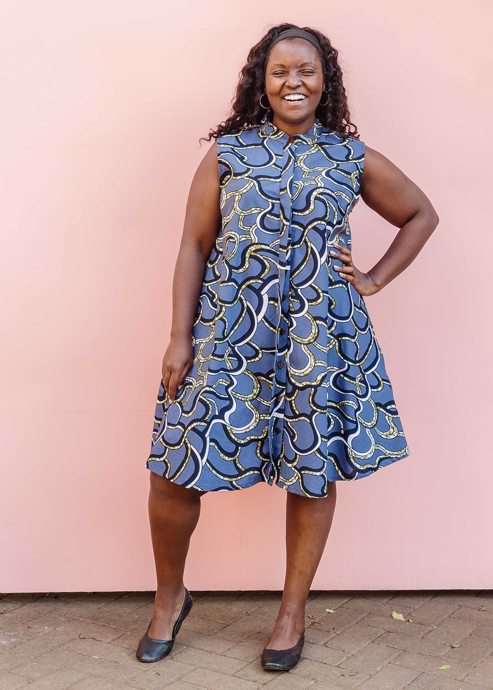 Model wearing blue sleeveless dress with green, white and navy squiggle design.