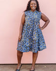 Model wearing blue sleeveless dress with green, white and navy squiggle design.