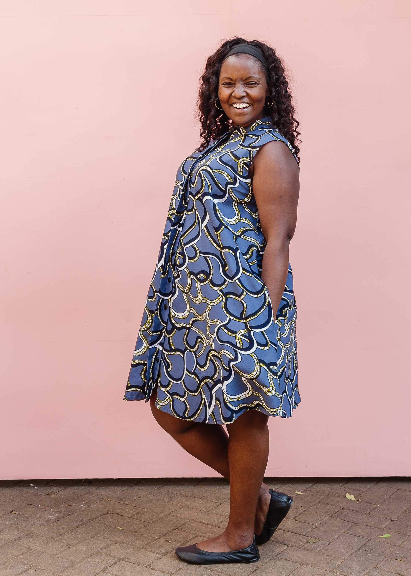 Model wearing blue sleeveless dress with green, white and navy squiggle design.