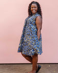 Model wearing blue sleeveless dress with green, white and navy squiggle design.