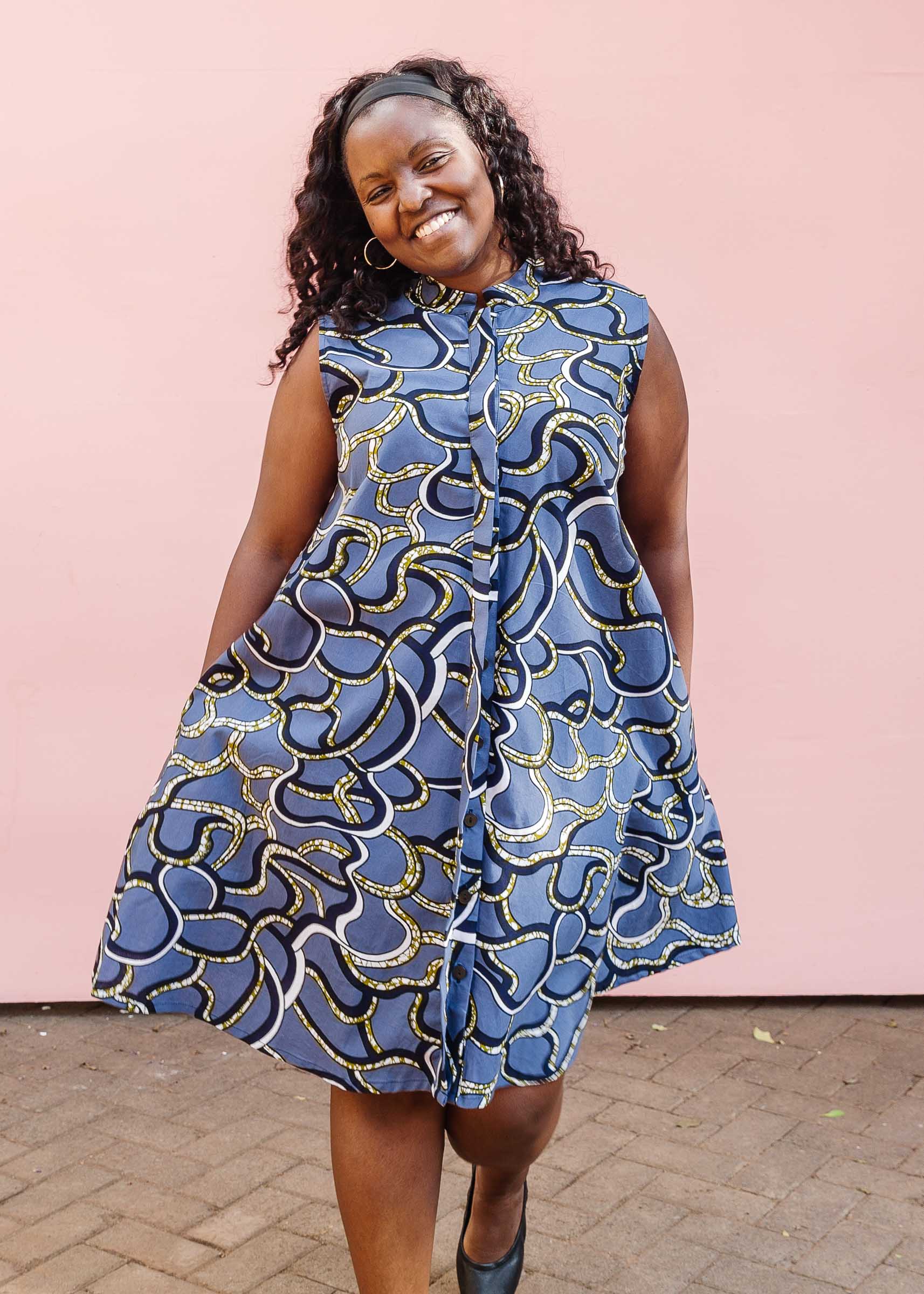 Model wearing blue sleeveless dress with green, white and navy squiggle design.