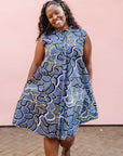 Model wearing blue sleeveless dress with green, white and navy squiggle design.