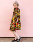 The model is wearing brown, yellow, red and black leaf print dress.