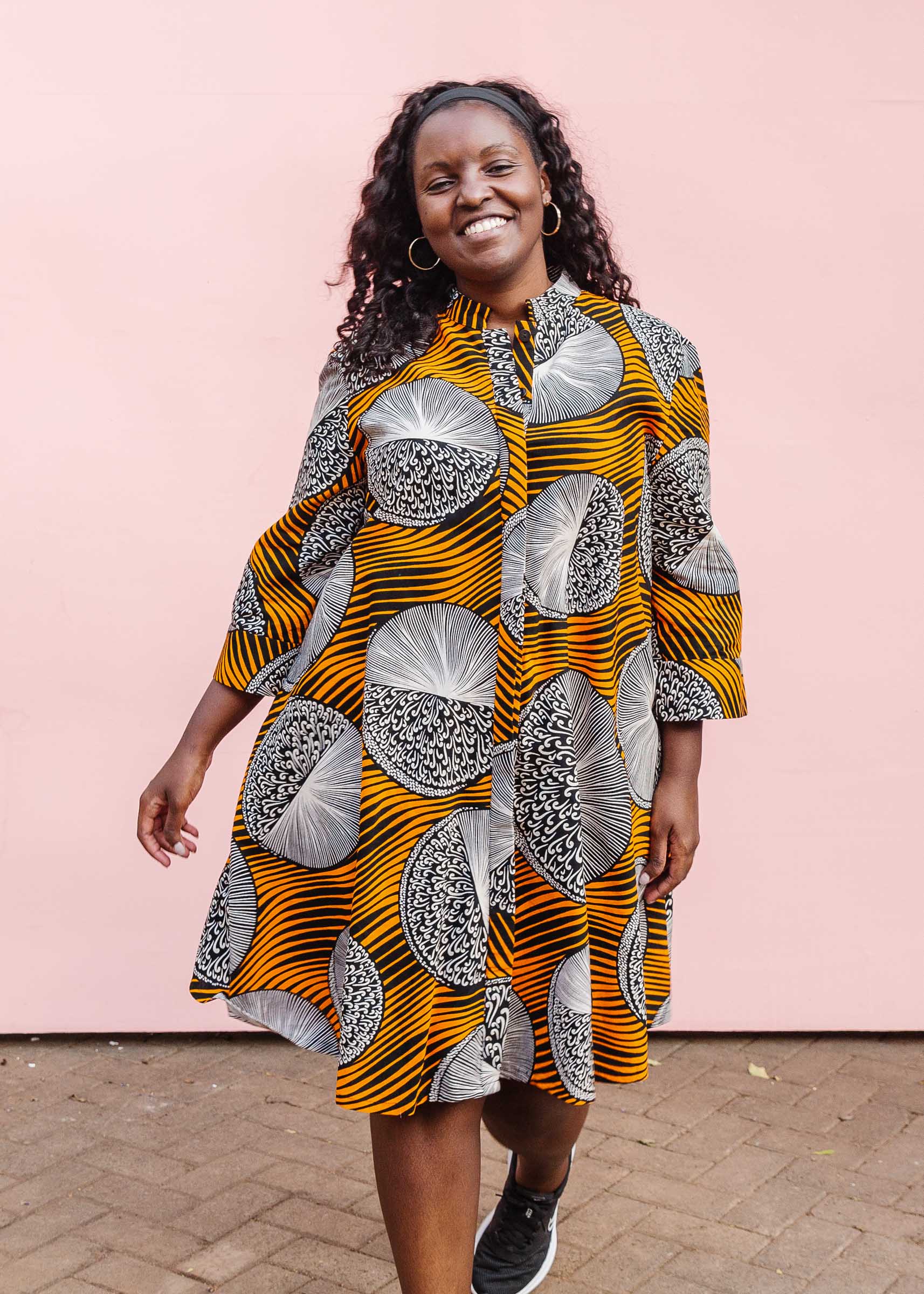 Model wearing black dress with orange stripes and black and white circles.