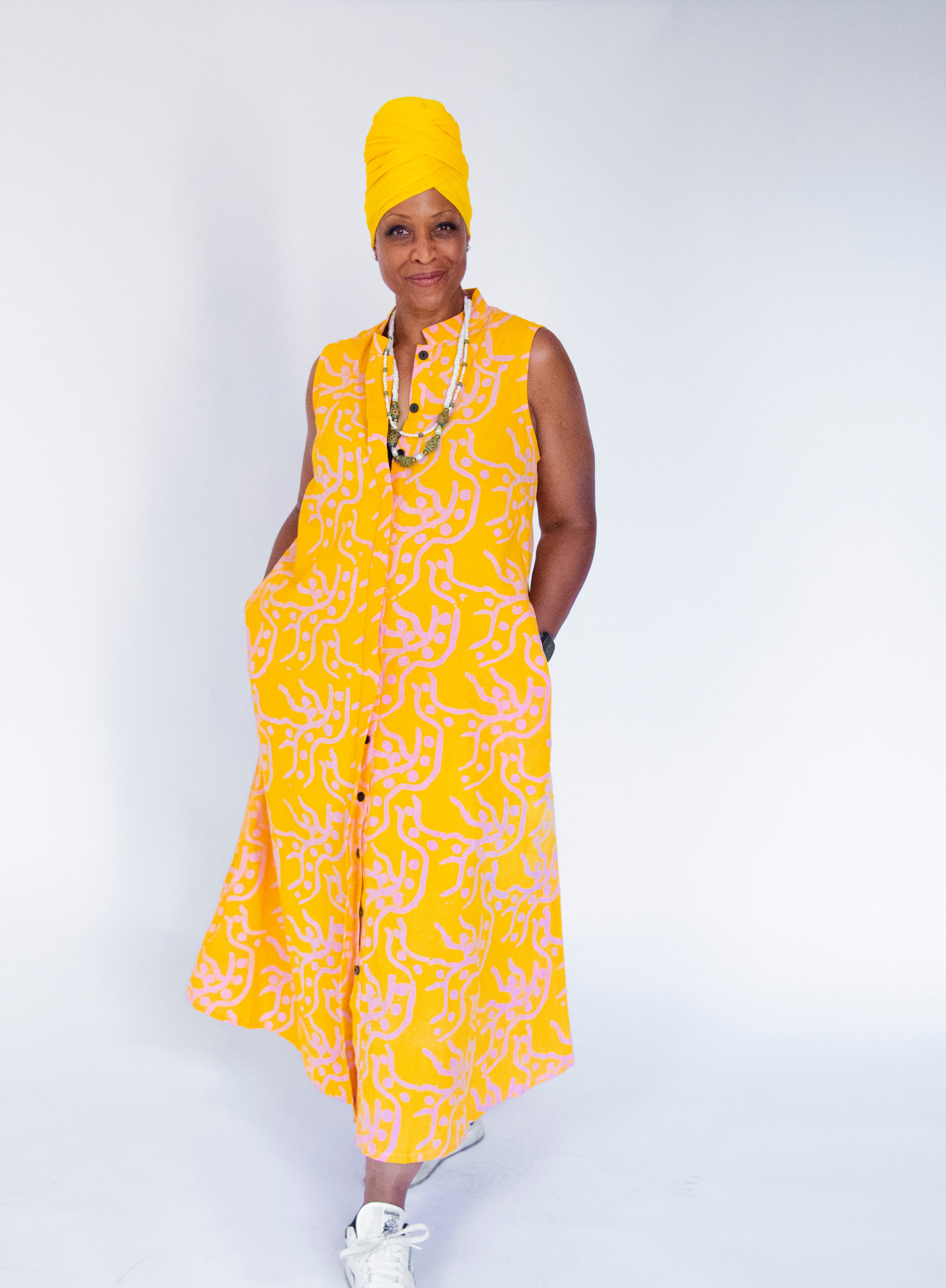 Model wearing yellow sleeveless dress with abstract pink print.