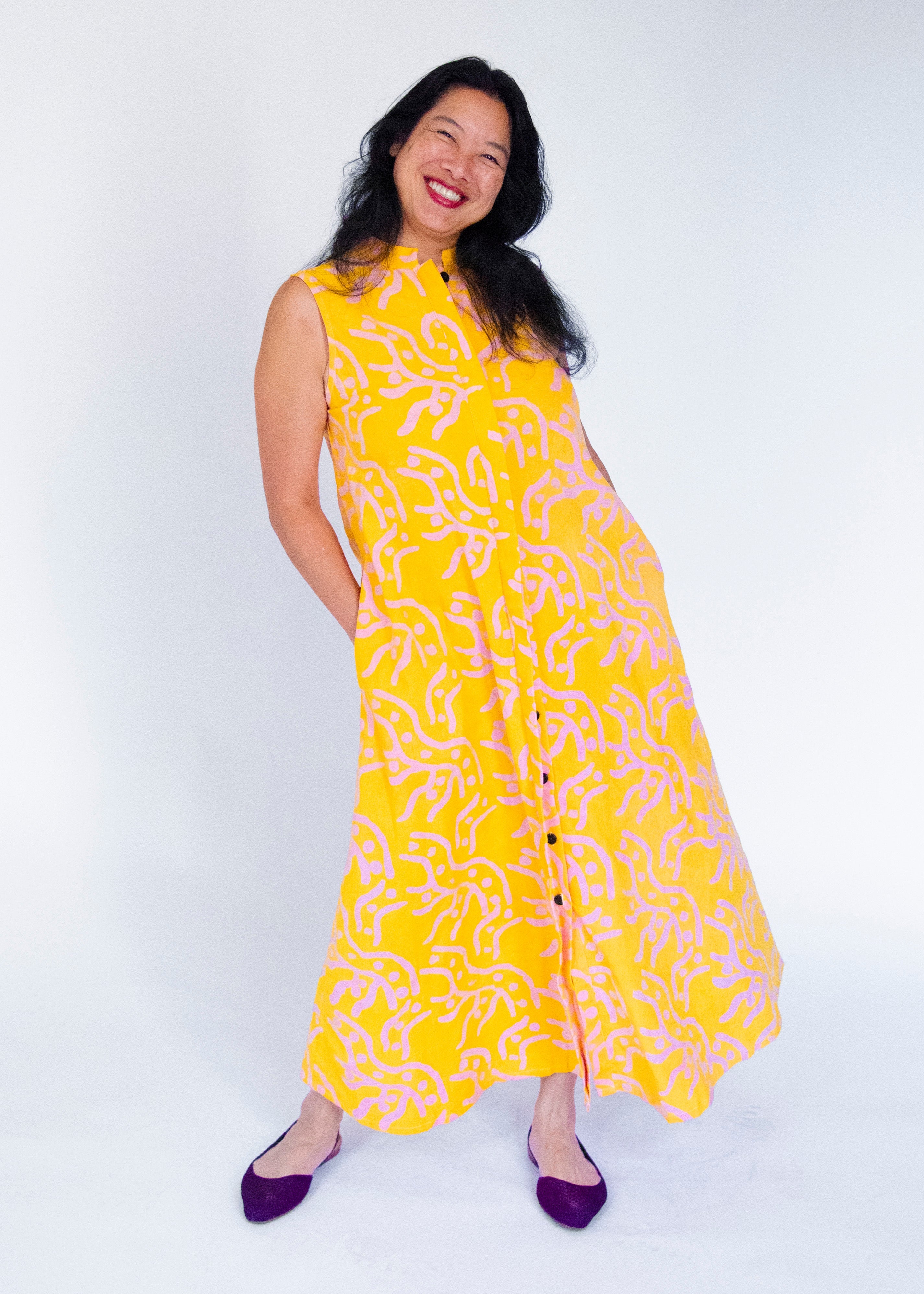 Model wearing yellow sleeveless dress with abstract pink print.