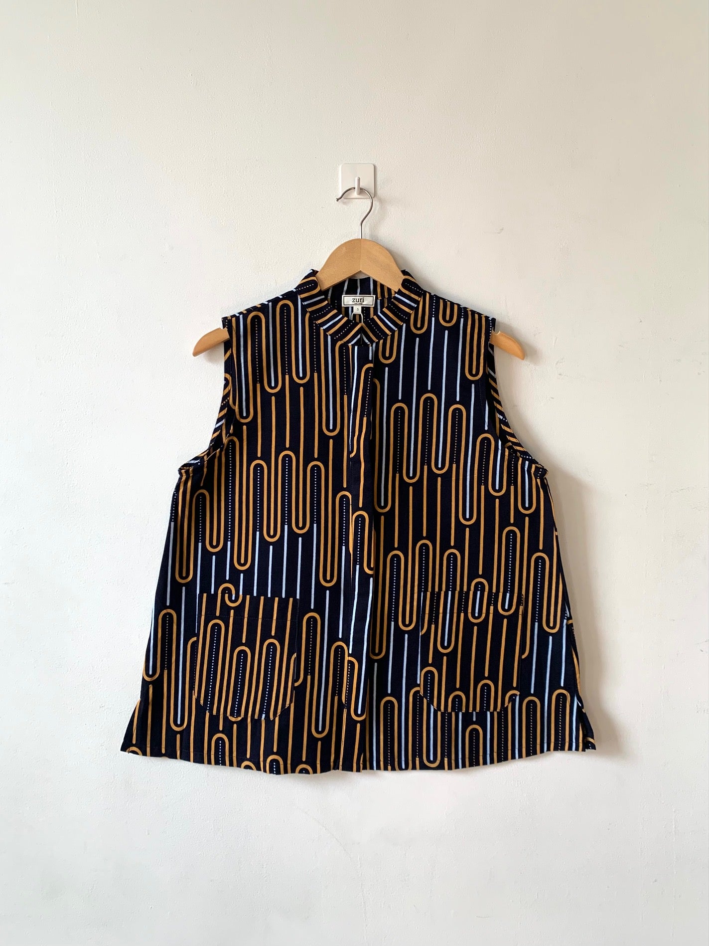 Display of sleeveless shirt with yellow and white geometric print.