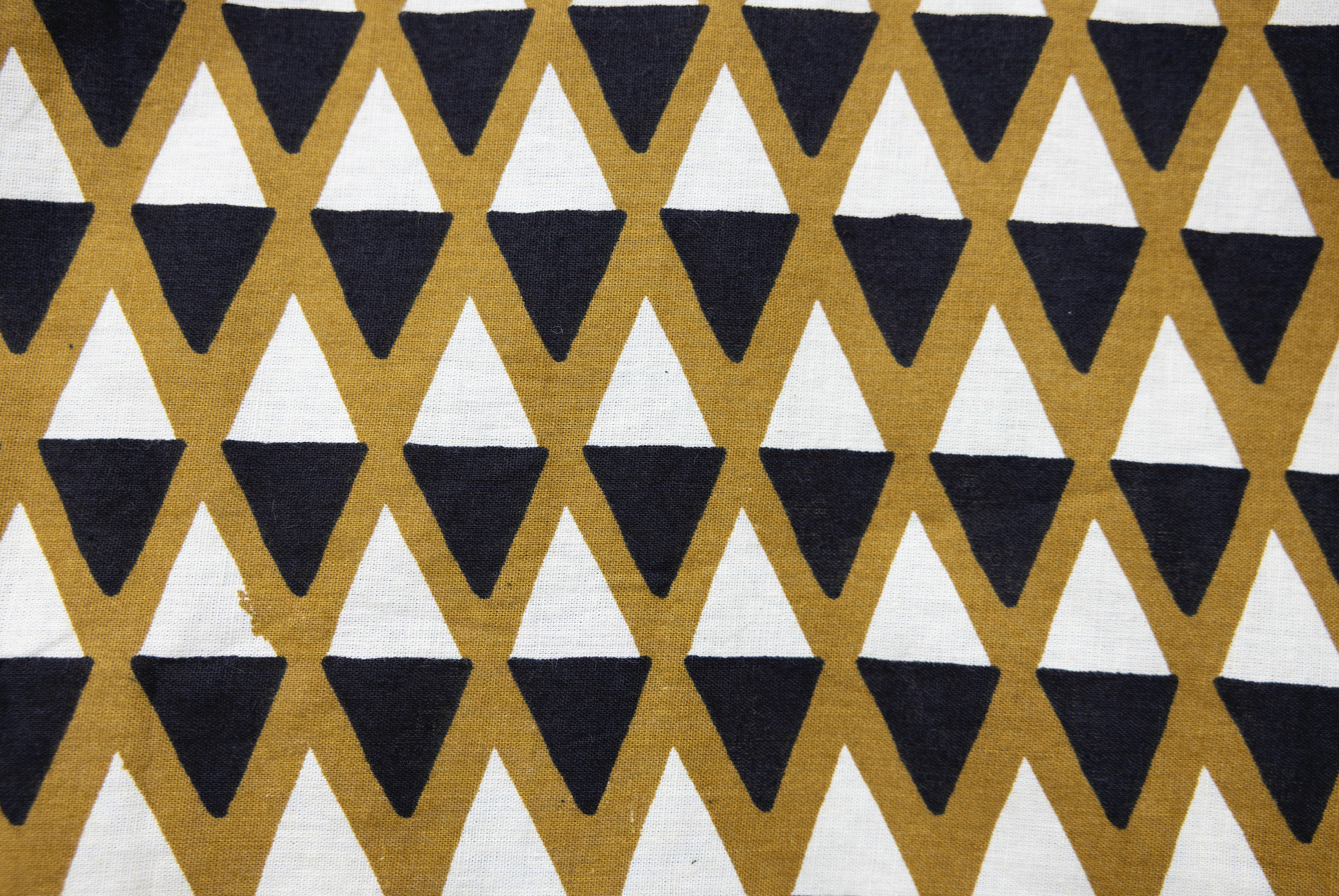 Close up display of mustard and black triangle print pants, fabric.