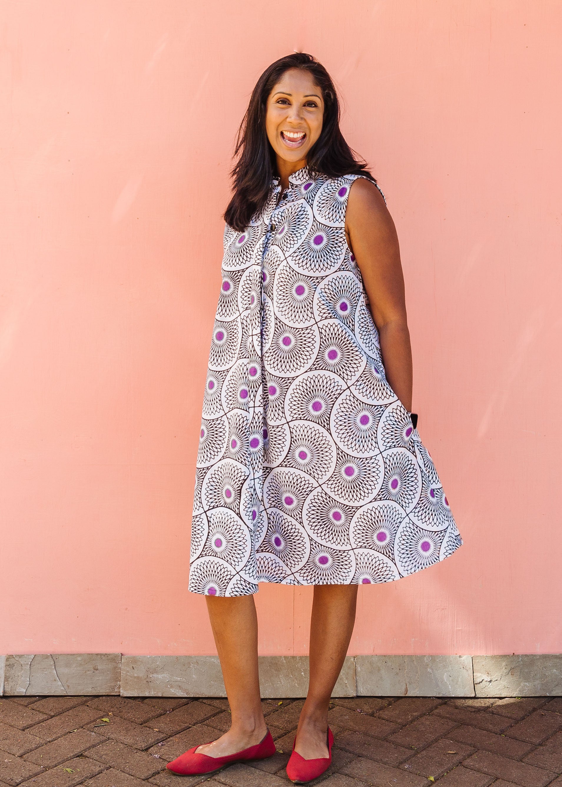 Model wearing white sleeveless dress with large black and purple floral print.