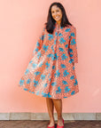 Model wearing orange dress with teal floral print.