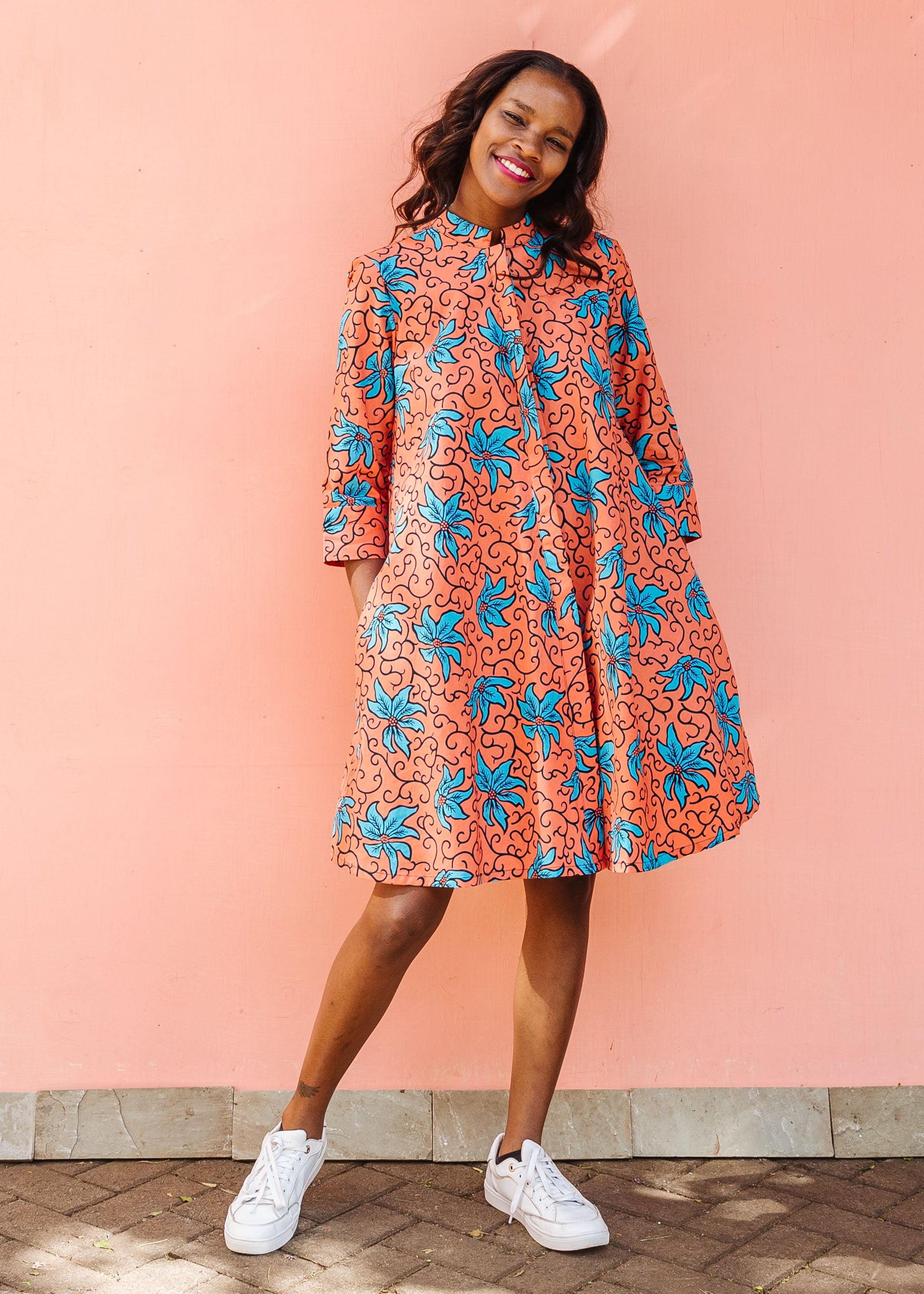 Model wearing orange dress with teal floral print.