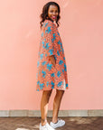 Model wearing orange dress with teal floral print.