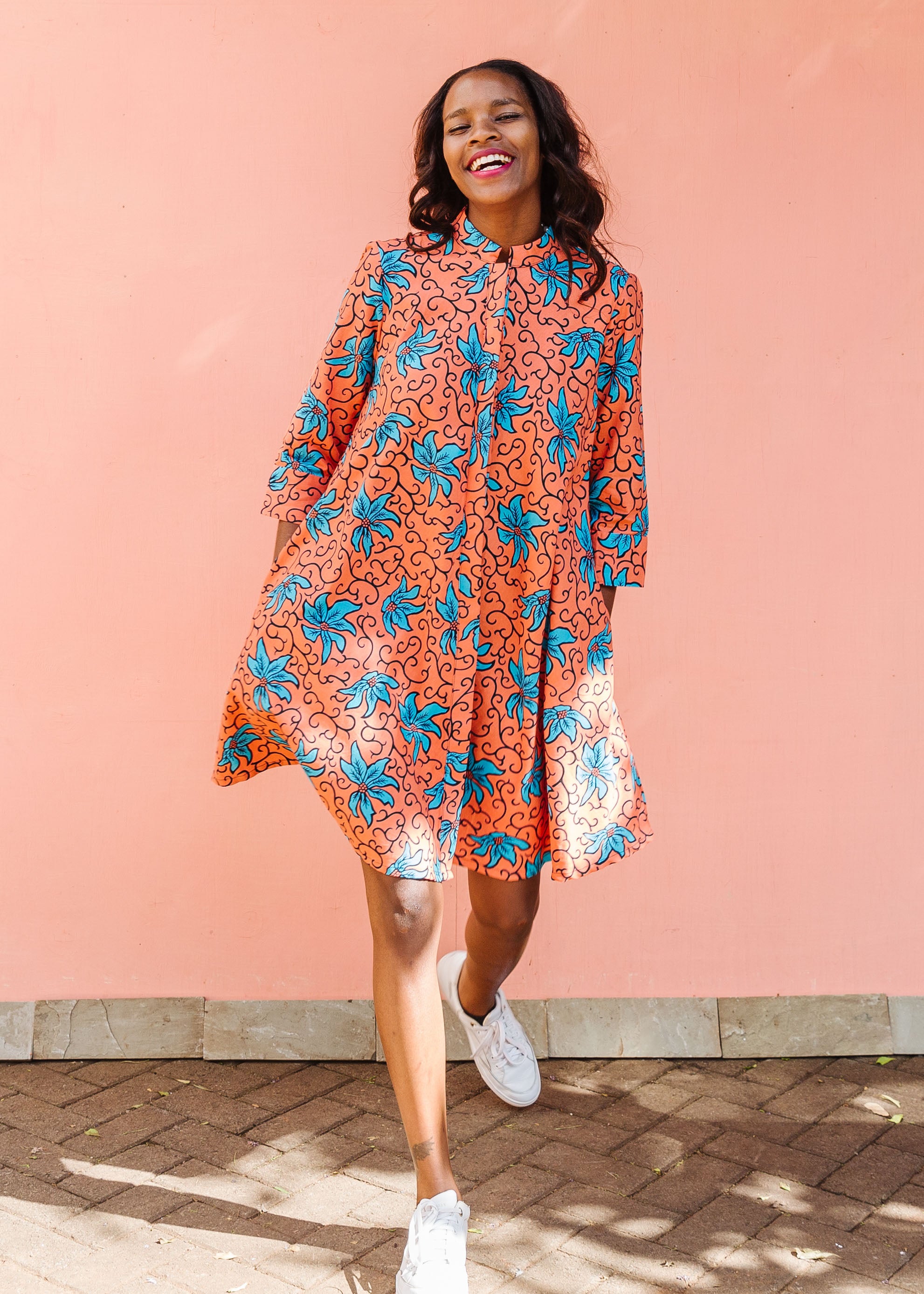 Model wearing orange dress with teal floral print.