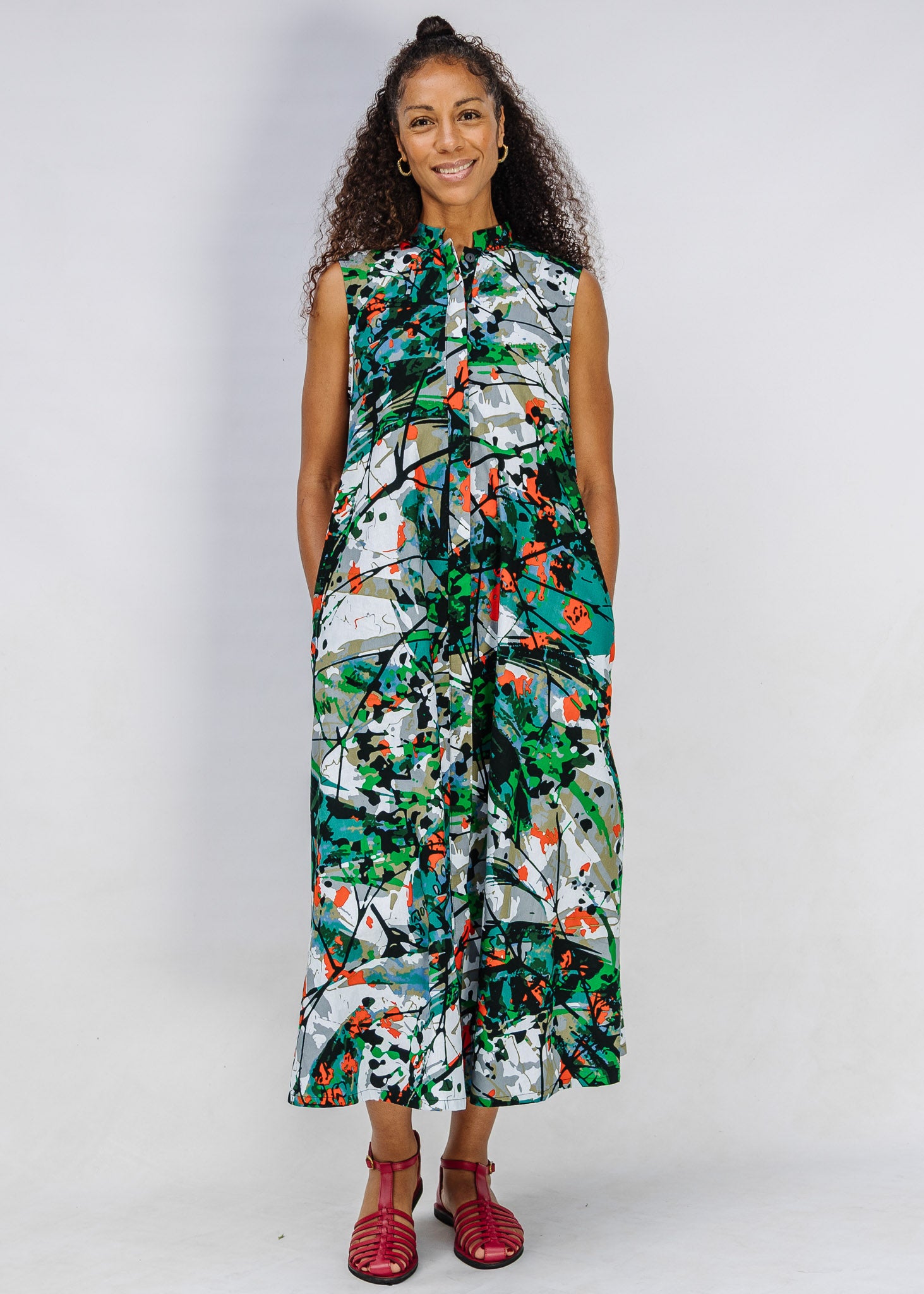 Model wearing dress with green, grey, white, orange and black abstract print.