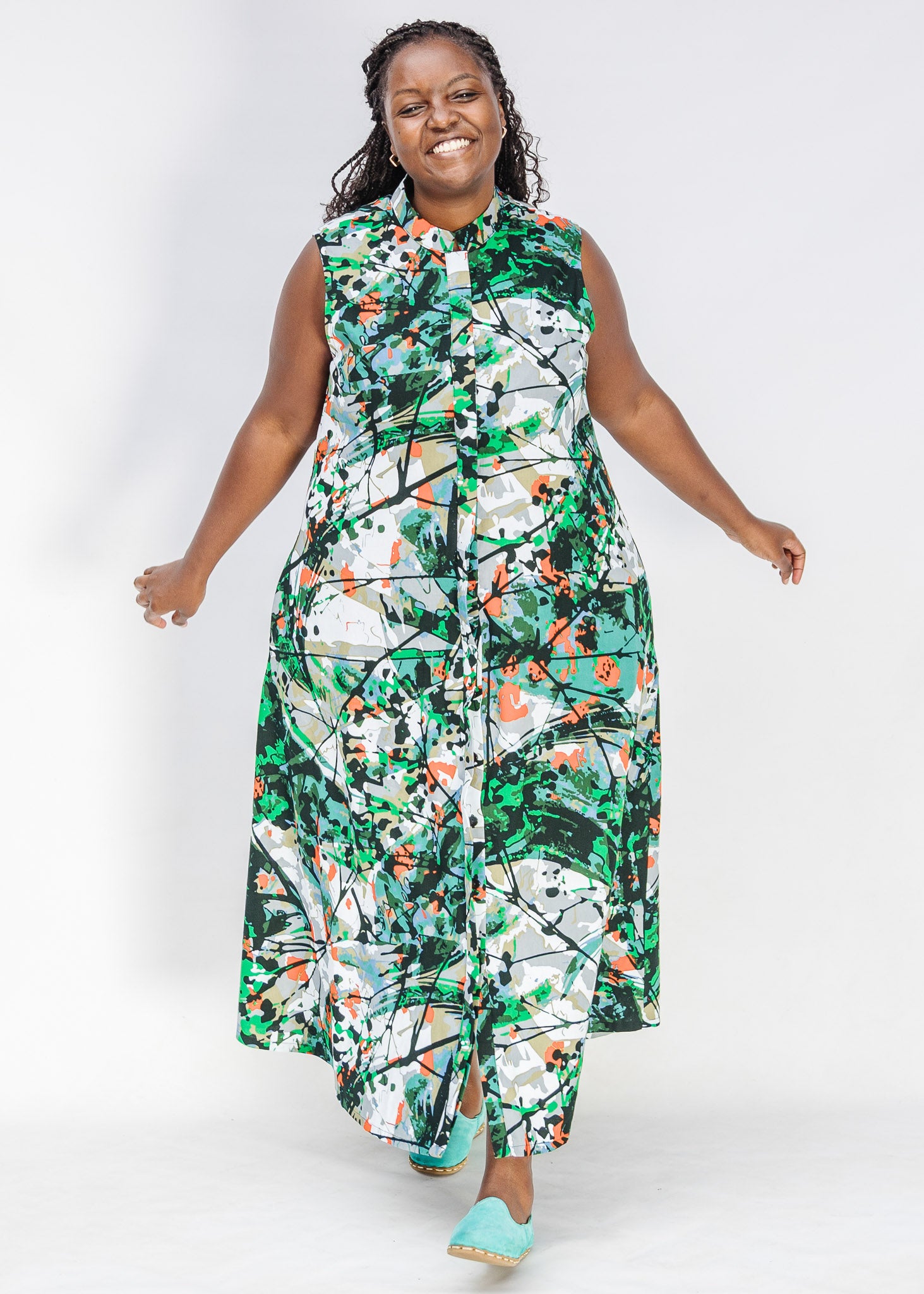 Model wearing dress with green, grey, white, orange and black abstract print.