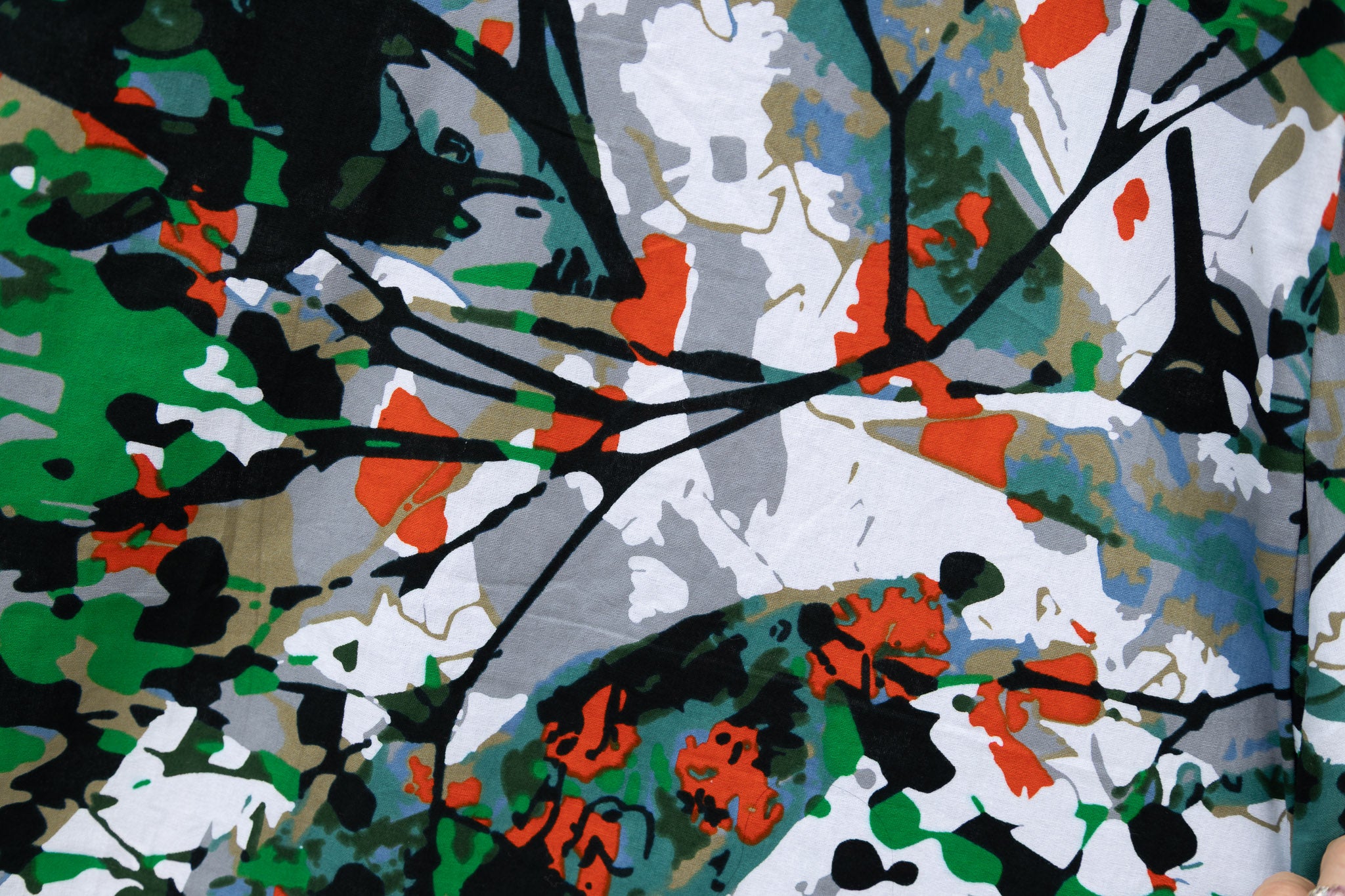 Close up display of dress with green, grey, white, orange and black abstract print, fabric.